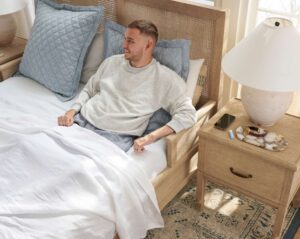 man in accessible bed leaning on bedrest and headboard propped up with pillows.